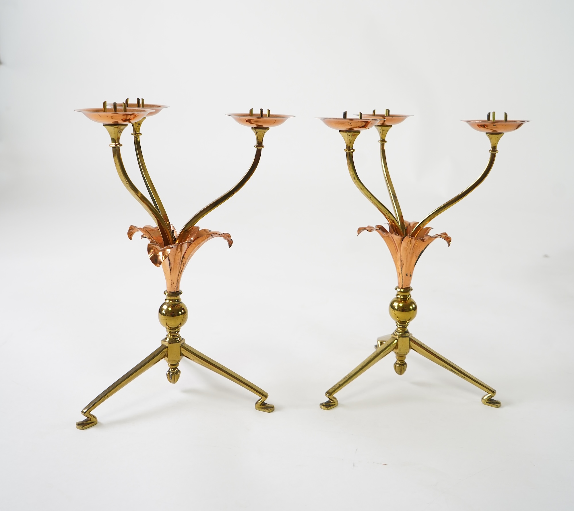 W.A.S. Benson & Co.: A pair of Arts and Crafts gilt brass and copper three branch candelabra
